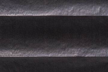 Close-up of black textured paper layers with horizontal lines and shadow play.