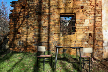 Partially ruined clay brick wall with a barred window underneath, an antique table and chairs, located in the Maragater&iacute;a region of Castile and Le&oacute;n, Spain