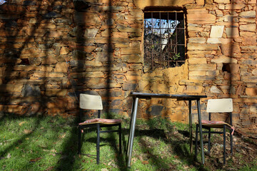 Partially ruined clay brick wall with a barred window underneath, an antique table and chairs, located in the Maragater&iacute;a region of Castile and Le&oacute;n, Spain