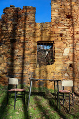 Partially ruined clay brick wall with a barred window underneath, an antique table and chairs, located in the Maragater&iacute;a region of Castile and Le&oacute;n, Spain