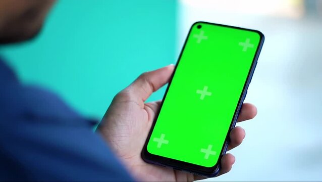 Person holding a smartphone with a green screen for easy content replacement, ideal for technology and app demonstrations.