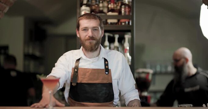 Watch a barman prepare a cocktail in a bar setting, showcasing skills and ingredients as he presents a drink to the camera for viewers to see