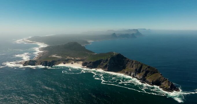 Wide Aerial view of Cape of Good Hope in South Africa. Dramatic cliffs at coastline, turquoise waters, sandy beach, and green terrain on sunny day. Ideal for travel and documentary use. 4K drone shot