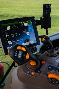 Close up of a John Deere tractor console shows dual joysticks, lit buttons, and a large touchscreen with rows guidance and hydraulic icons, indicating automated steering.