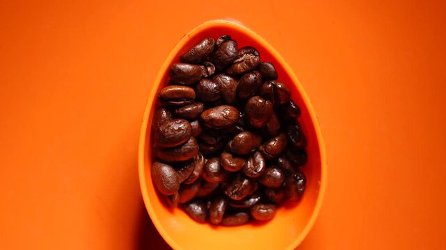 Scoop of whole bean coffee rotating orange color background top down