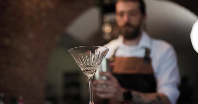 Bartender Pours Cocktail From Shaker Into Martini Glass in a Stylish Bar Setting