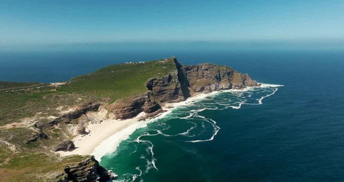 Aerial zoom in drone footage of the Cape of Good Hope peak, showcasing rugged cliffs, vivid greenery, and coastal scenery on a sunny day. Ideal for travel, nature, landscape, and documentary projects