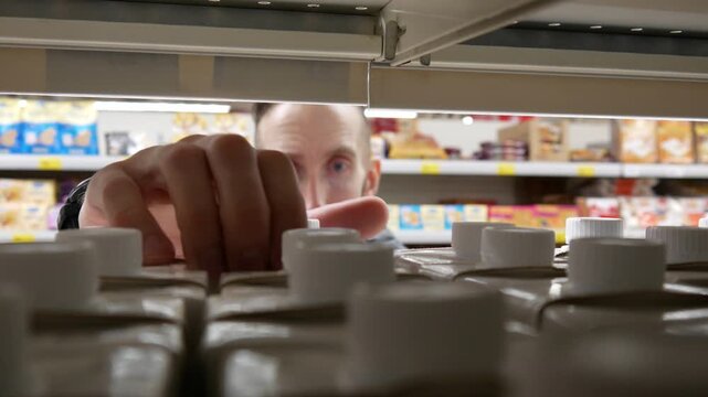 A male consumer selects a carton of milk drink or juice in a supermarket aisle