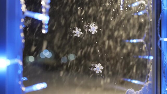Slow motion view of gentle white snow falling softly outside a window pane bordered by glowing blue and white LED icicle lights exterior, window, flurry