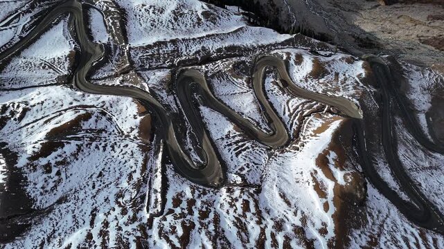 Winding mountain road switchbacks through snowy hills aerial view