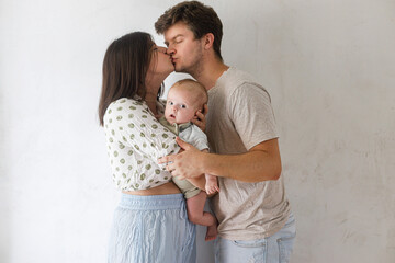 Happy parents holding newborn baby in room. Mother and father hugging and kissing, holding sweet infant. Adoption, love and family concept