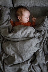Adorable baby sleeping in brown sheets on bed, top view. Nap time. Sweet newborn baby in parents bed sleeping. Love and care concept