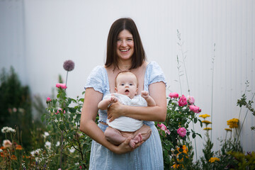 Happy mother holding newborn baby in summer garden. Mom hugging son and smiling with sweet infant outdoors. Happy mothers day! Adoption, love and family concept