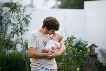 Young father holding newborn baby in summer garden. Dad hugging son and kissing sweet infant outdoors. Happy fathers day! Adoption, love and family concept