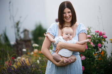 Happy mother holding newborn baby in summer garden. Mom hugging son and smiling with sweet infant outdoors. Happy mothers day! Adoption, love and family concept