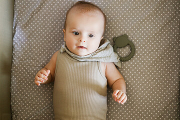 Cute happy baby lying in crib with teether, top view with coy space. Teething. Sweet infant portrait in grey bassinet with silicone toy. Childhood, Love and care concept.