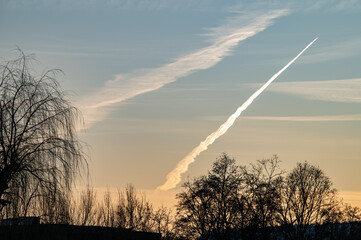 Silhouetten laublose B&auml;ume vor abendlichem Himmel mit Abendrot und Kondenstreifen in Neckartenzlingen.