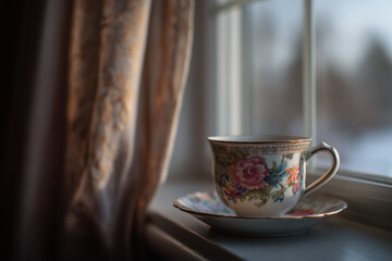 Elegant tea cup with floral design placed on a saucer by the window