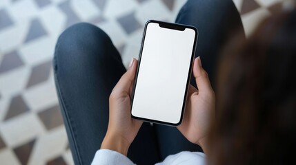 Woman sits in a chair holding a blank screen mock up mobile phone, preparing for a digital task in a cozy indoor space during daytime