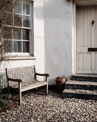 Rustic wooden bench outside white cottage entrance with vintage door and climbing vines