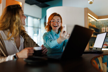 Businesswomen engage in lively conversation and collaboration at a modern office space with laptops and coffee, promoting teamwork and innovation during a productive day