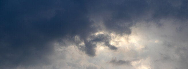 Dramatic dark storm sky with dense black clouds and bright light through clouds, atmospheric weather background before thunderstorm