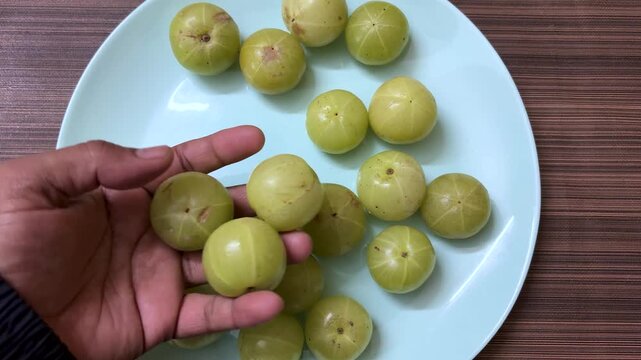 hand holding fresh indian gooseberry amla on plate top view indoor