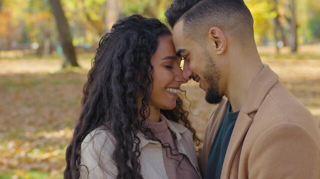 Dreamy Hispanic couple looking away touching foreheads kissing noses smiling Arabian man Caucasian woman multiethnic people in love family dating in autumn fall park city relationship partners happy