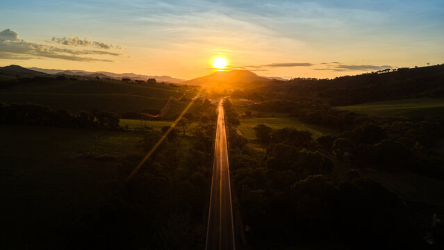 Uma rodovia em Minas Gerais com um belo p&ocirc;r do sol e montanhas com fazendas ao longo da estrada.