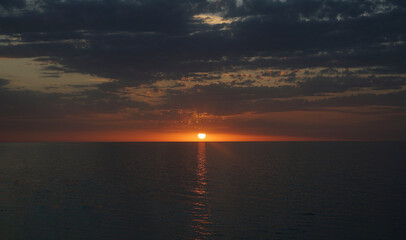 The glowing disk nears the ocean's boundary, quickly fading behind the horizon line, sending out its last rays over a large reef area. Caspian Sea Aktau Kazakhstan