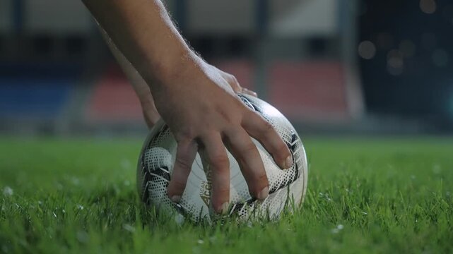 A footballer's hands place the ball on the turf of a football field before a shot