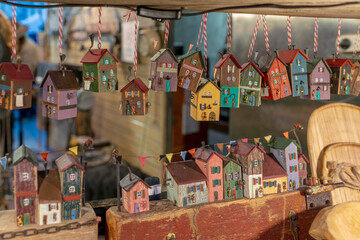 Obraz premium Colorful tiny wooden house ornaments hang on strings above a display of rustic miniature buildings. Cozy handmade decor for home, gift, and seasonal market vibes with shallow depth of field.