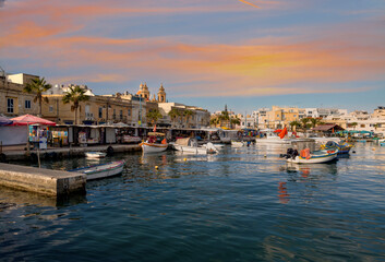 Fototapeta premium Marsaxlokk harbor scene with fishing boats, market stalls and church dome