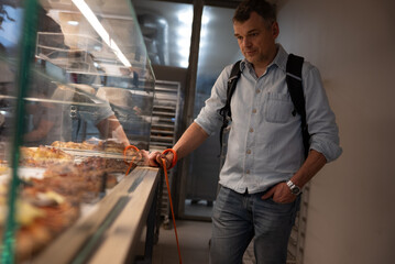 Man holding dog leash standing in bakery looking at pastry display
