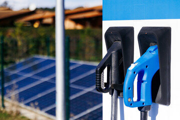 Electric vehicle charging station with two charging connectors, solar panels in the background, showcasing renewable energy and sustainable transportation solutions