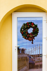 Festive Christmas Wreath On Glass Door Against Yellow Wall With Balcony View