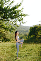 Fototapeta premium Young woman practicing yoga outdoors, showcasing flexibility and balance in a serene green setting, reflecting calmness and health