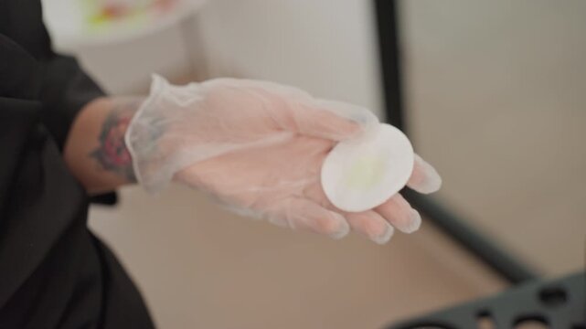 stylist applying hair dye with gloves, closeup of applicator brush and cotton pad, foil highlights in client hair, careful sectioning, precise pigment placement, professional studio setting