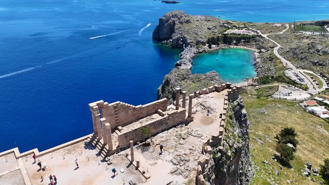 Aerial drone video of iconic archaeological site of Acropolis of Lindos built uphill featuring picturesque village, amazing organized beach and Saint Paul bay, Rhodes island, Dodecanese, Greece
