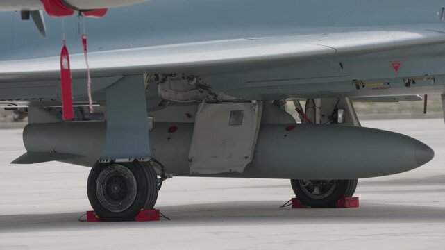 Underside view of main landing gear and paired external fuel tanks on military transport aircraft with chocks