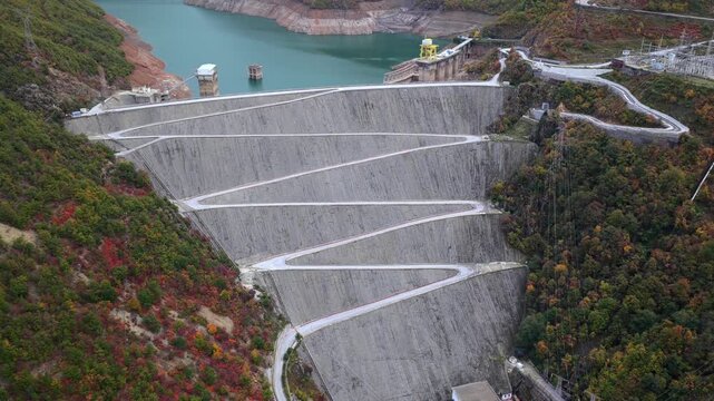 Aerial video of the Fierz&euml; dam rising above autumn hills and the turquoise reservoir in Northern Albania. 
