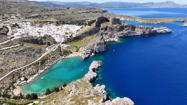 Aerial drone cinematic video of stunning crystal clear sea and small organized beach of Saint Paul's bay overlooked by Acropolis of Lindos, Rhodes island, Dodecanese, Greece