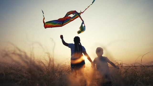 Two children flying kite in field. Young girl flying kite in field at sunset. A boy holding fun hands outdoors. A pair of kids flying a kite in a meadow lifestyle.