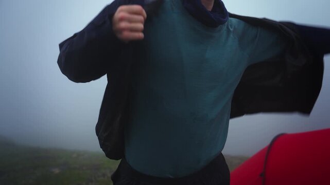 Hiker Putting on Shell Jacket Near Tent in Fog