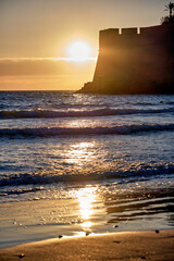 Sunset over Pe&ntilde;iscola beach with castle silhouette and waves reflecting light on water surface