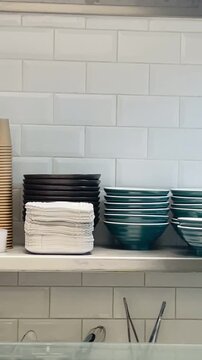 stacked plates cups on tiled shelf neat rows of ceramic bowls, porcelain dishes, paper takeaway cups, folded napkins and serving utensils Vertical, taken on the mobile device.