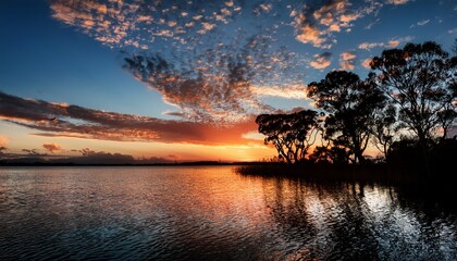 Dramatic Sunset Over Water With Silhouetted Trees And Dynamic Cloud Formations