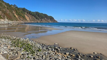 Serene ocean coastline with sandy beach and rocky shoreline on a clear day. Asturias, Spain. Tourism, vacation, travel concept. Concha de Artedo beach.