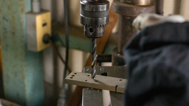 Drill press drilling holes in metal part at manufacturing workshop