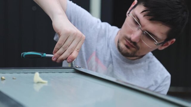 A brunette guy installing fasteners using a ratchet wrench.